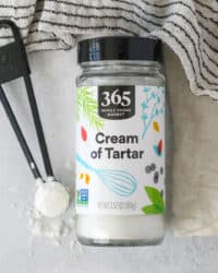 Overhead view of a jar of cream of tartar laying on a countertop next to a teaspoonful.