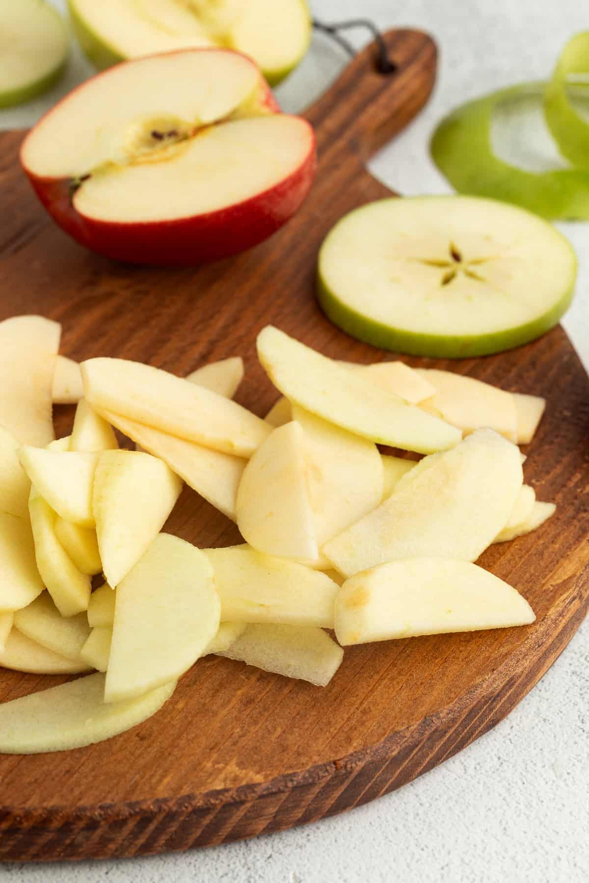 Sliced Granny Smith and Gala apples on a wooden cutting board, with apples cut in half in the background.