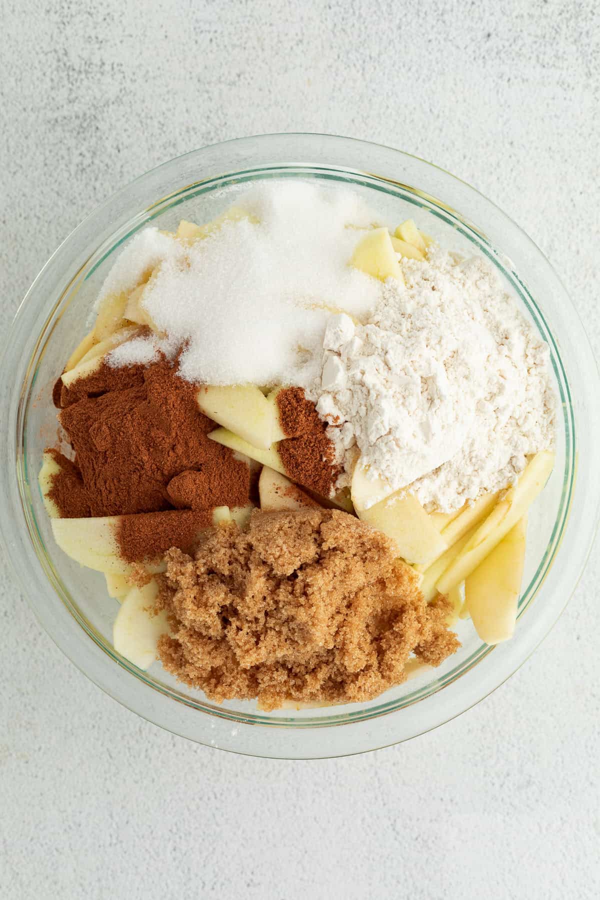 Apple pie filling ingredients combined in a glass bowl.