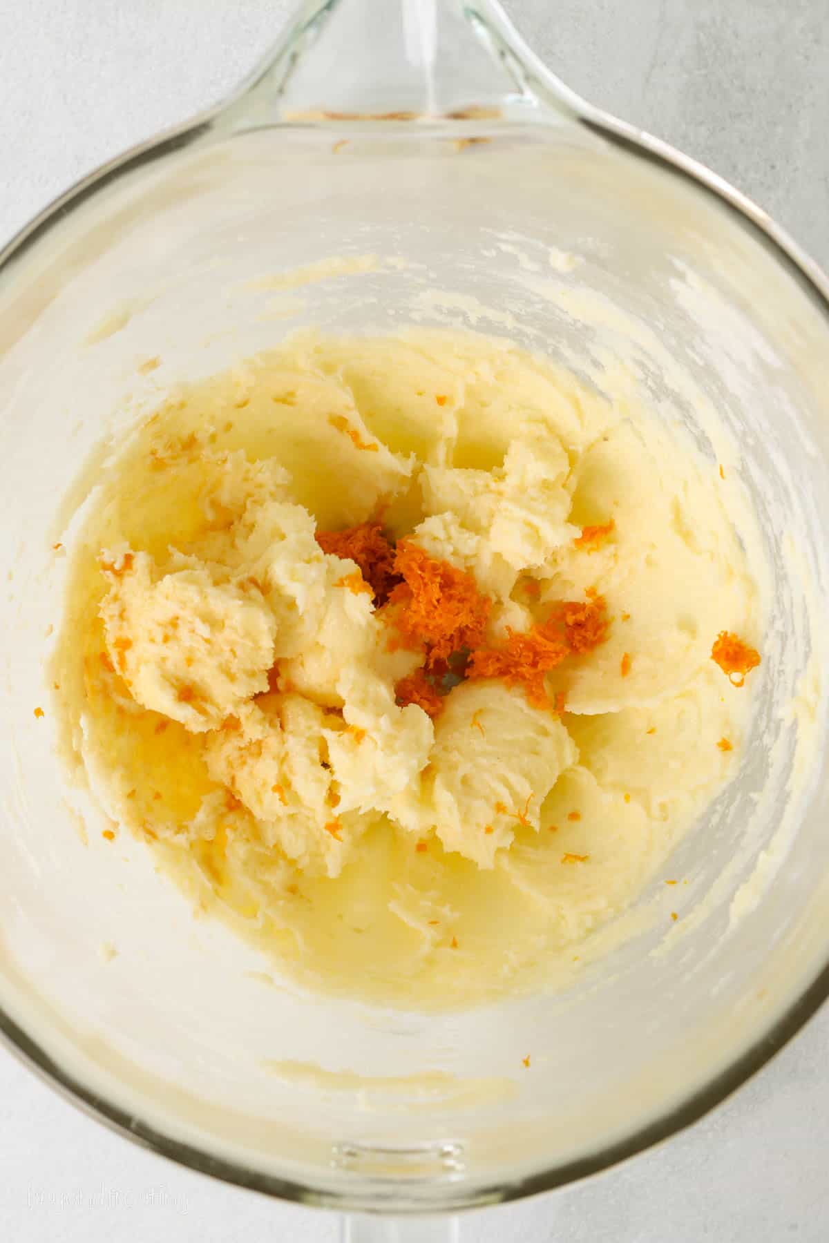 Orange zest added to shortbread cookie dough in a glass mixing bowl.