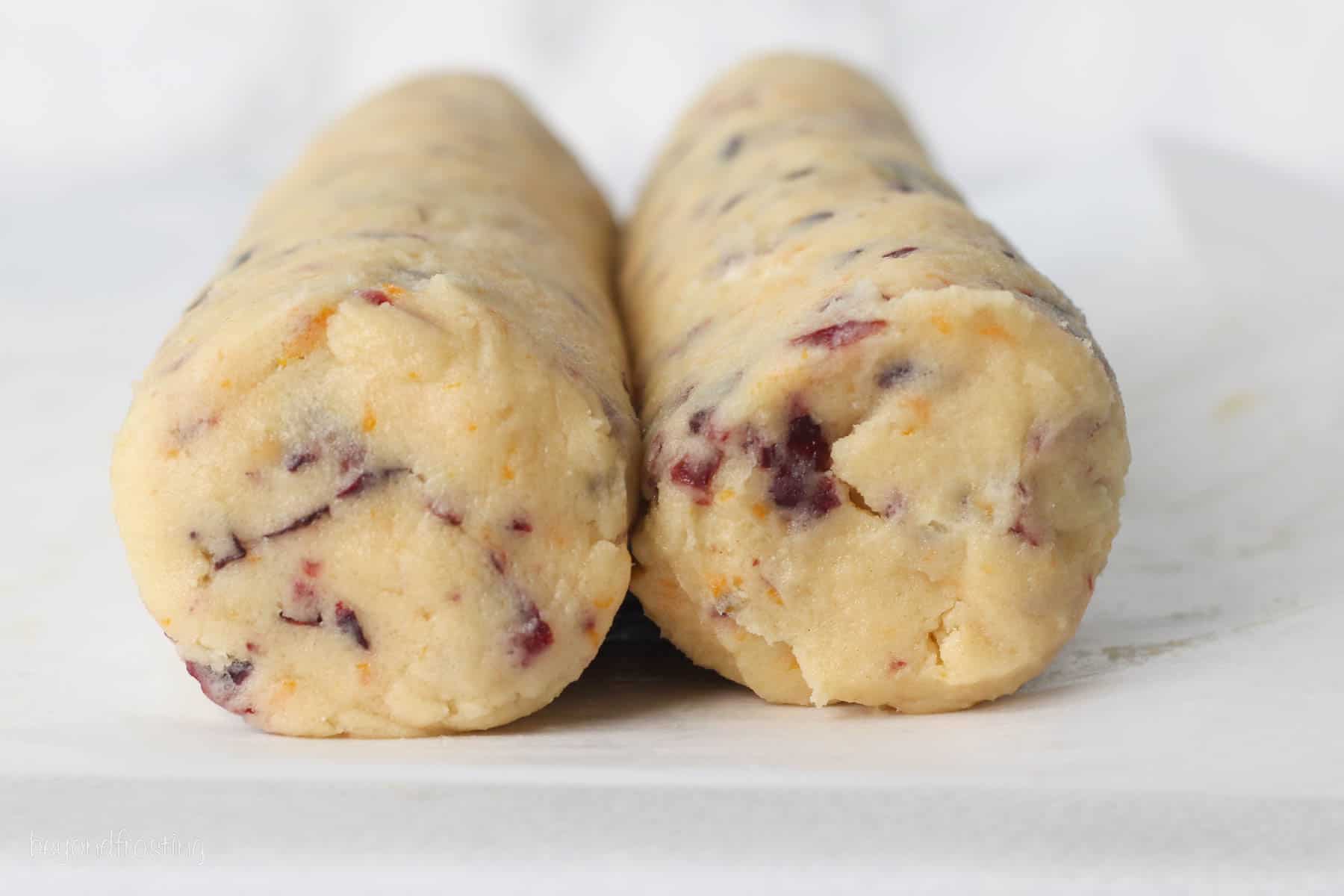 Two logs of cranberry orange shortbread cookie dough resting side-by-side on a countertop.