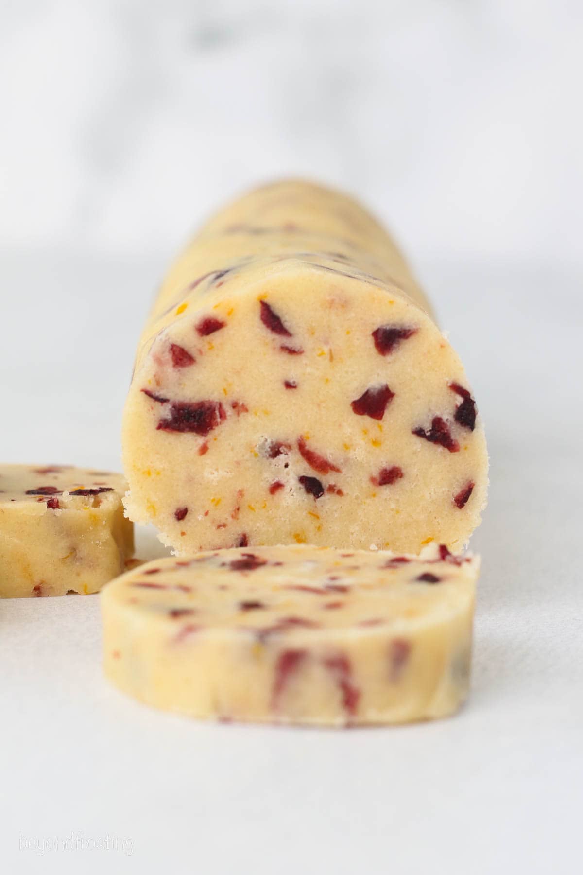 A log of cranberry orange shortbread cookie dough with a slice cut from the end.