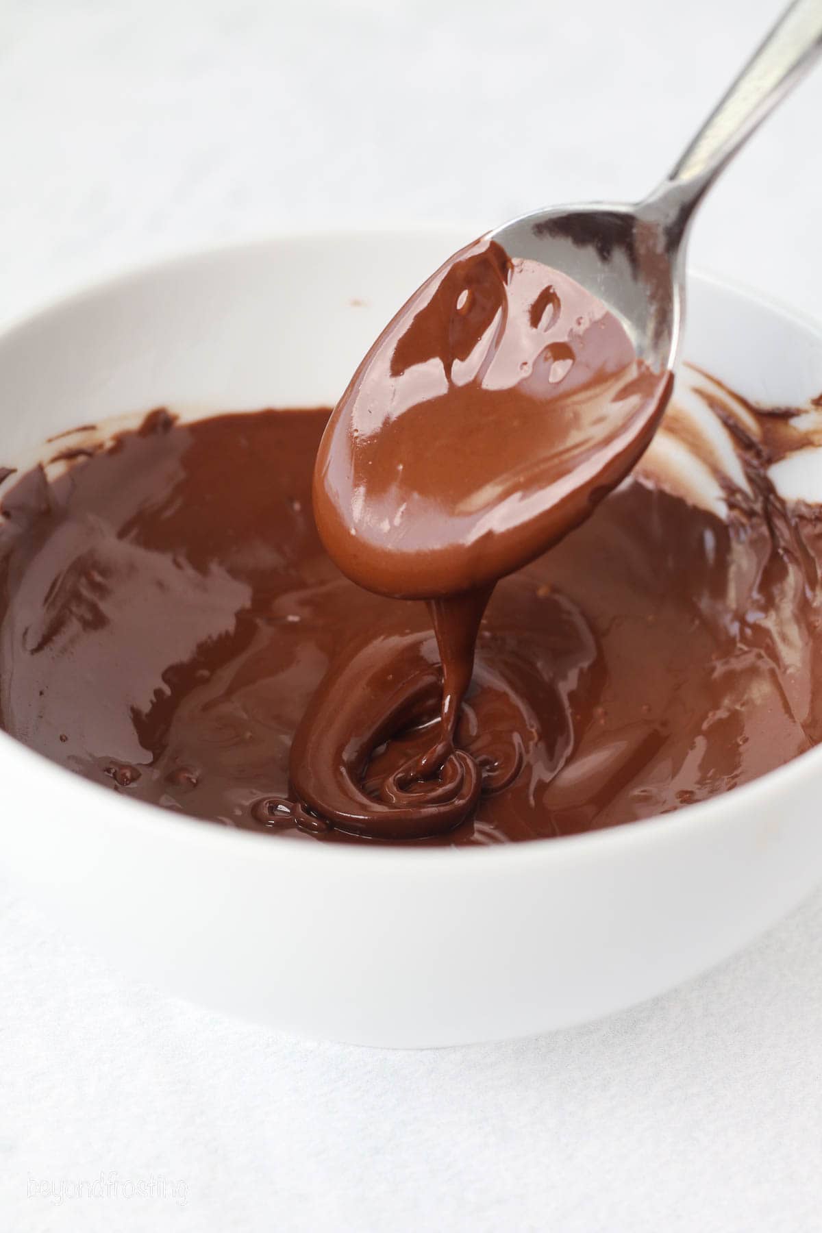 A spoon dipped into a bowl of melted chocolate.