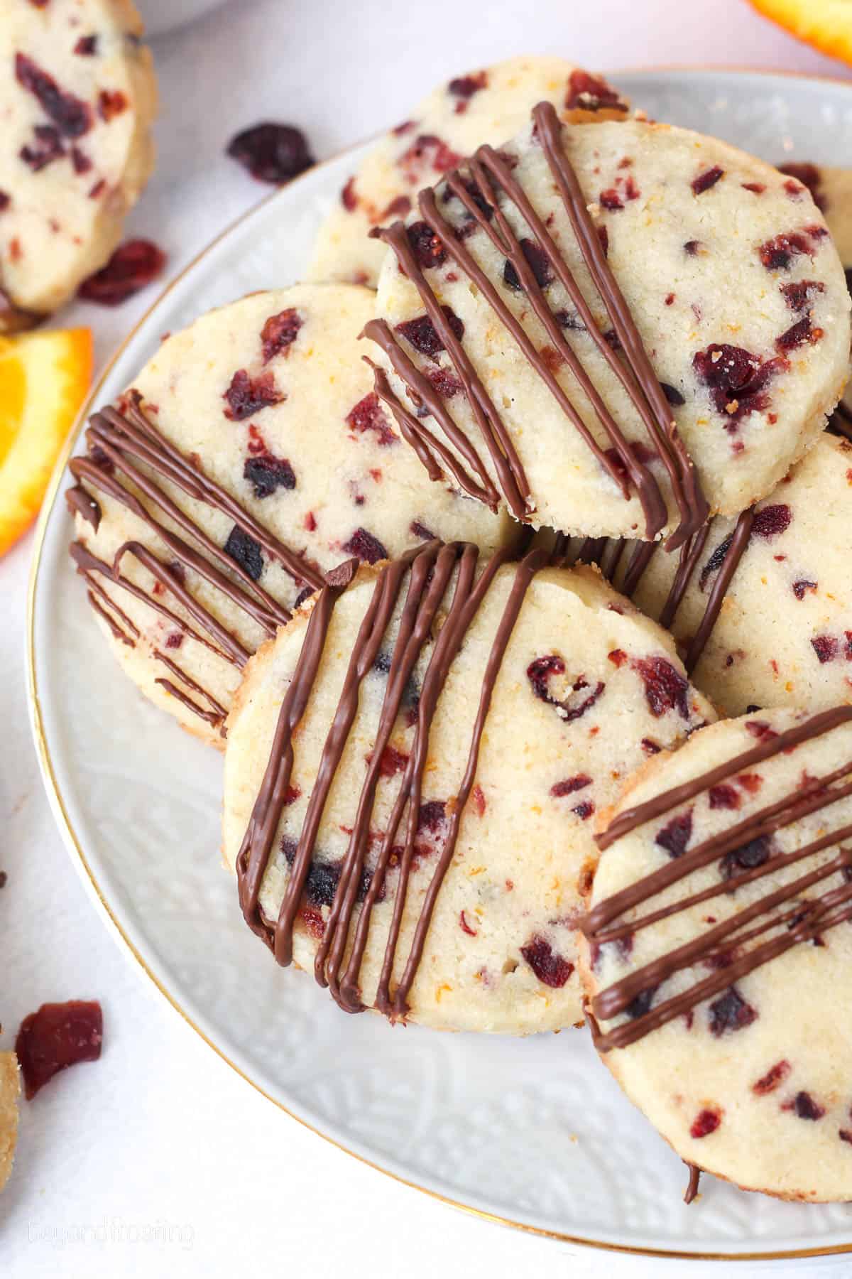 Cranberry orange shortbread cookies drizzled with melted chocolate, stacked on a white plate.