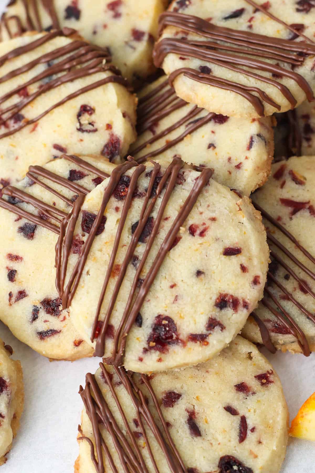 Close up of cranberry orange shortbread cookies drizzled with melted chocolate, stacked on a white plate.