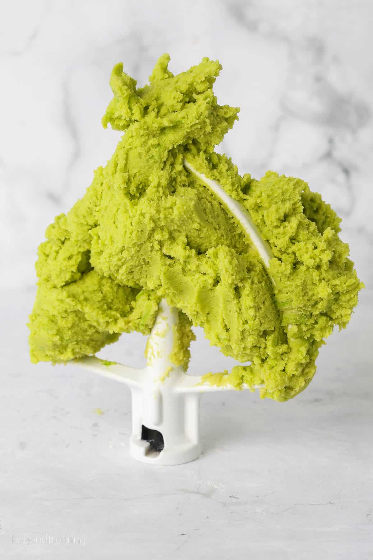 Green sugar cookie dough clumped on a stand mixer attachment.
