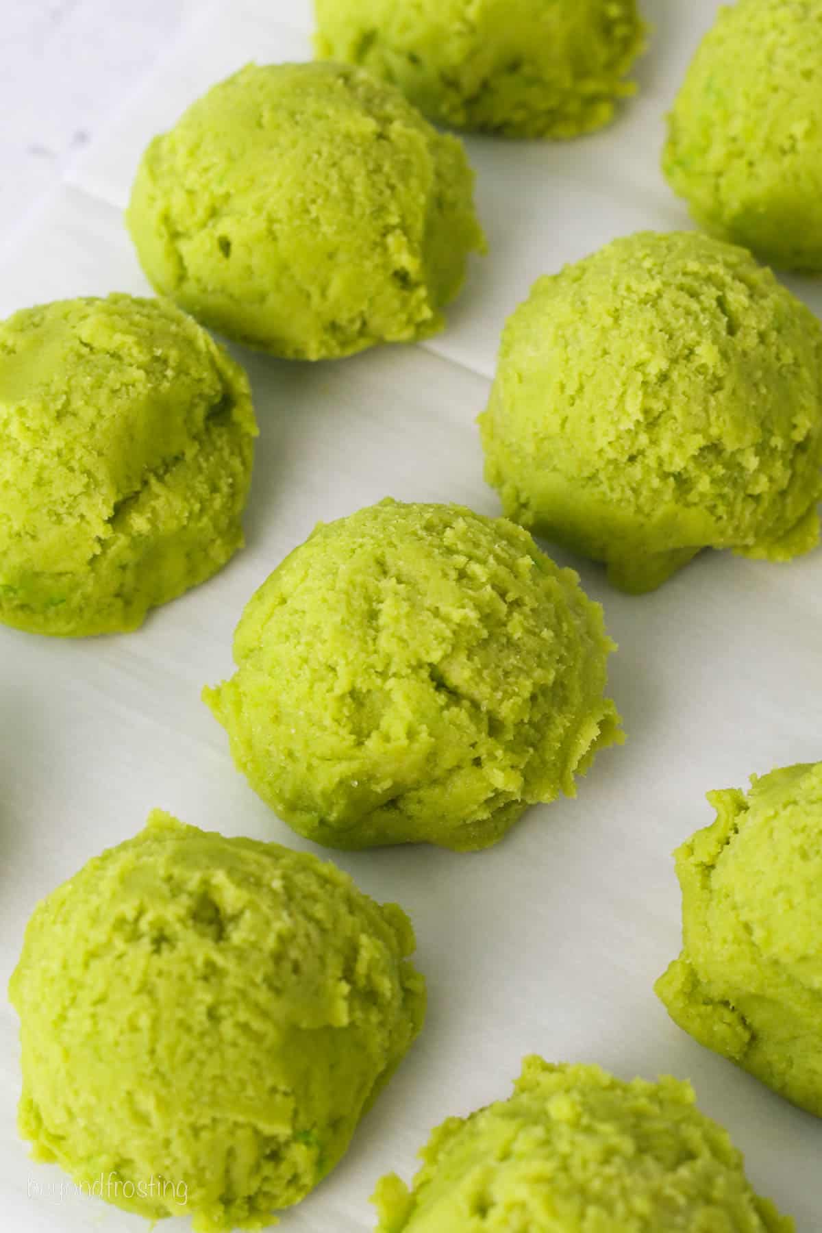 Rows of scoops of green sugar cookie dough on a baking sheet.