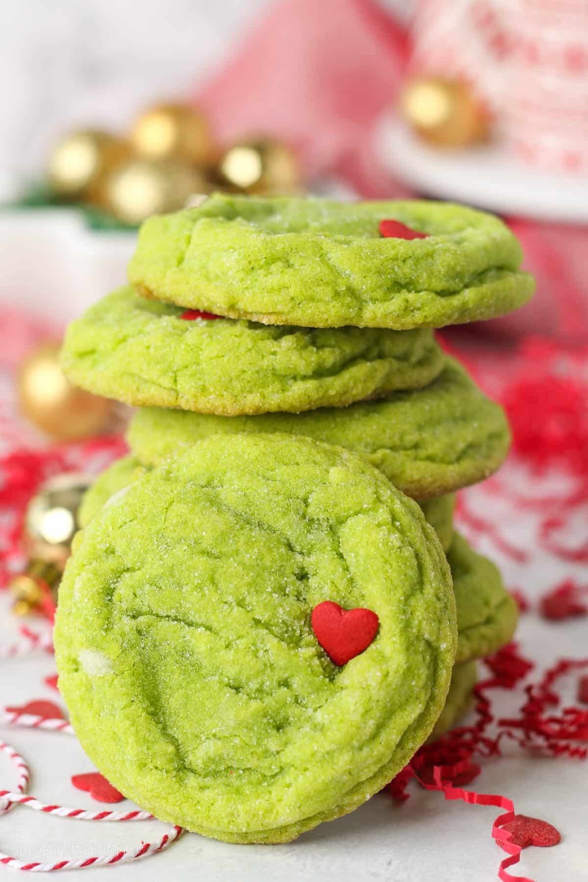 Close up of a stack of grinch cookies on a countertop surrounded by festive holiday decorations.