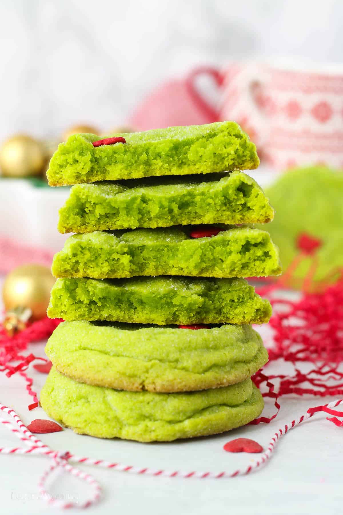 A stack of grinch cookie halves on a countertop with holiday decorations in the background.