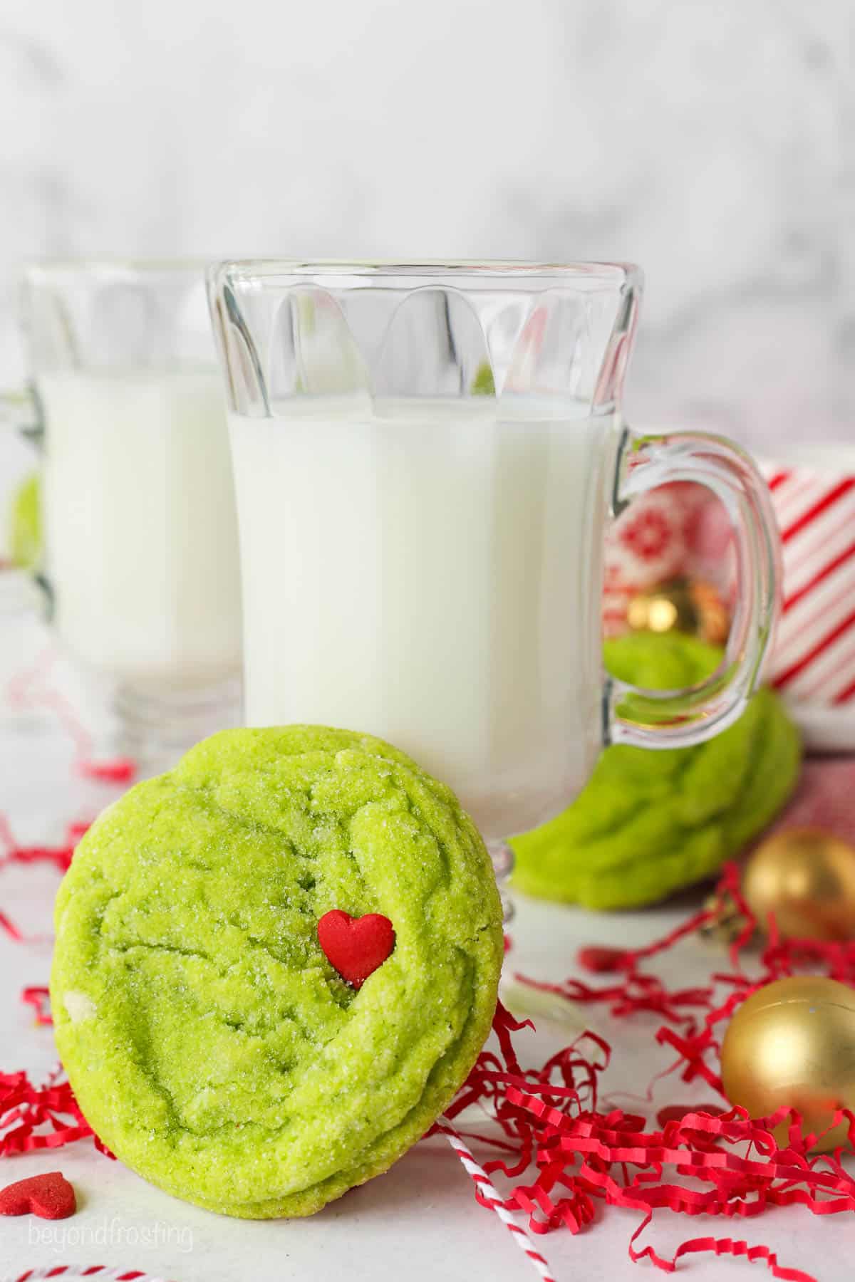 A glass of milk with a grinch cookie leaning up against it.