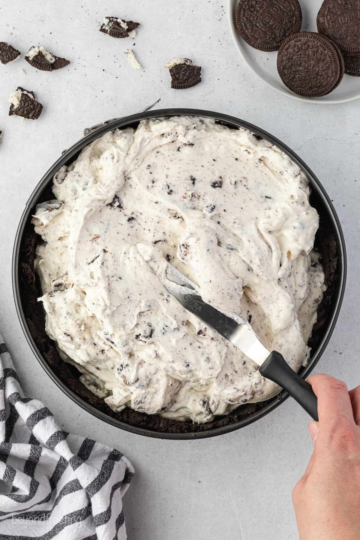 A spatula spreading Oreo cheesecake batter in a prepared springform pan