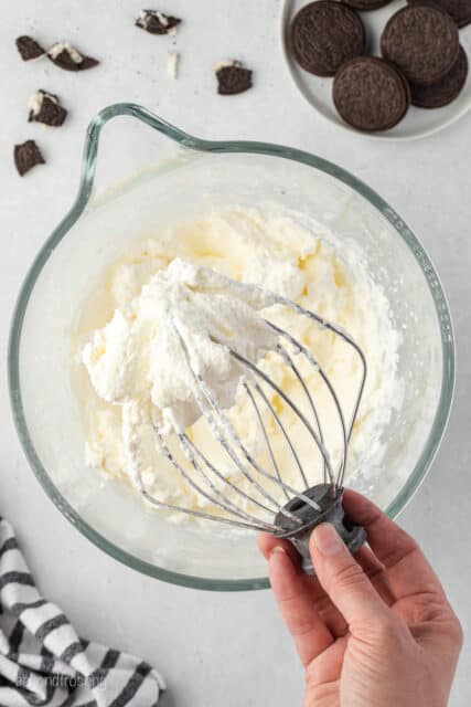 A hand holding a whisk attachment with whipped cream