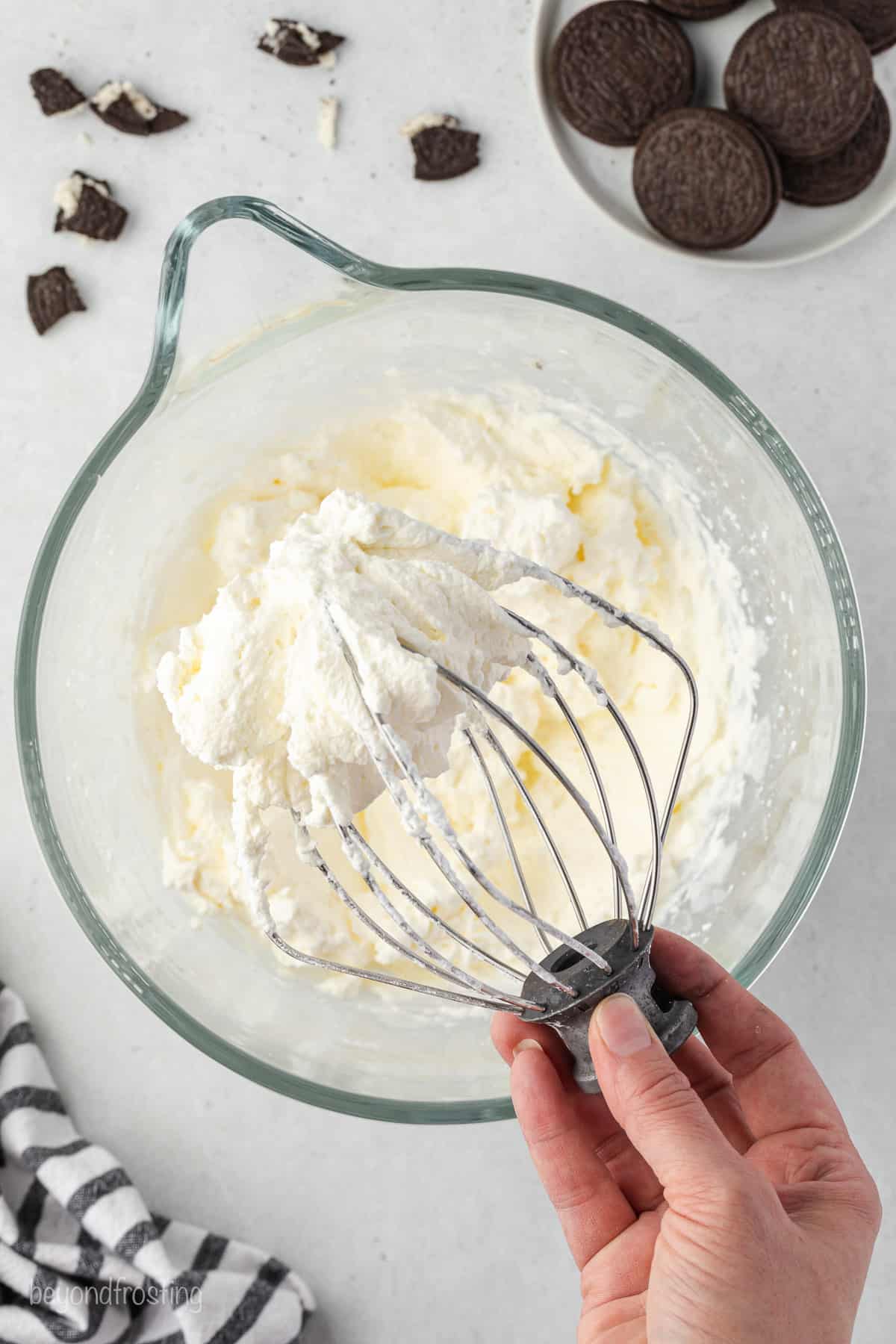 A hand holding a whisk attachment with whipped cream