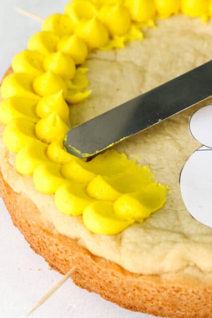Close up of yellow buttercream pedal frosting technique on a cookie cake with an angled spatula
