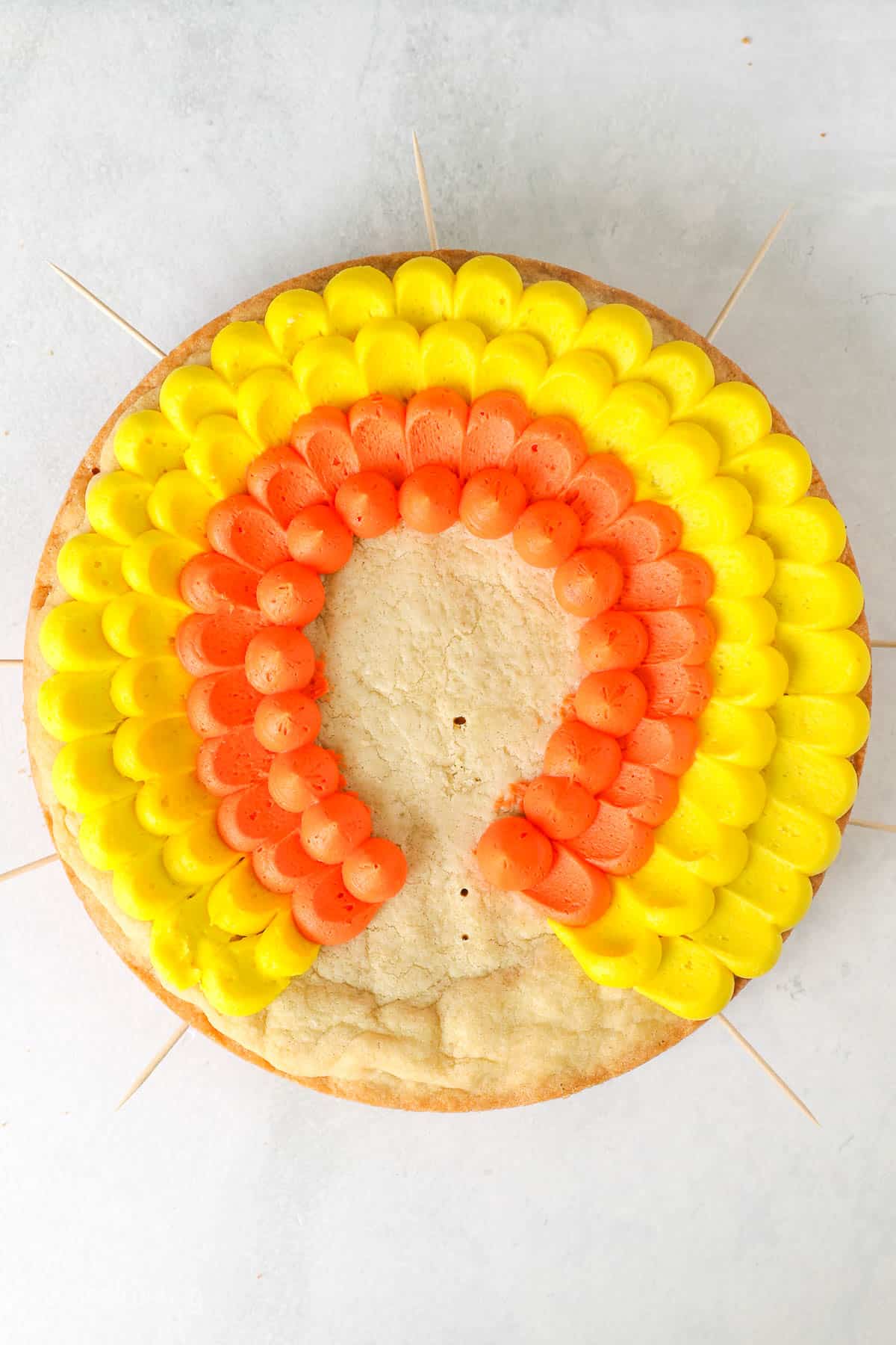 Overhead view of a cookie cake with a rows of yellow and orange frosting to make turkey feathers