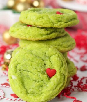 Close up of a stack of grinch cookies on a countertop surrounded by festive holiday decorations.