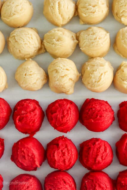 Overhead view of rows of white and red sugar cookie dough balls on a white surface.