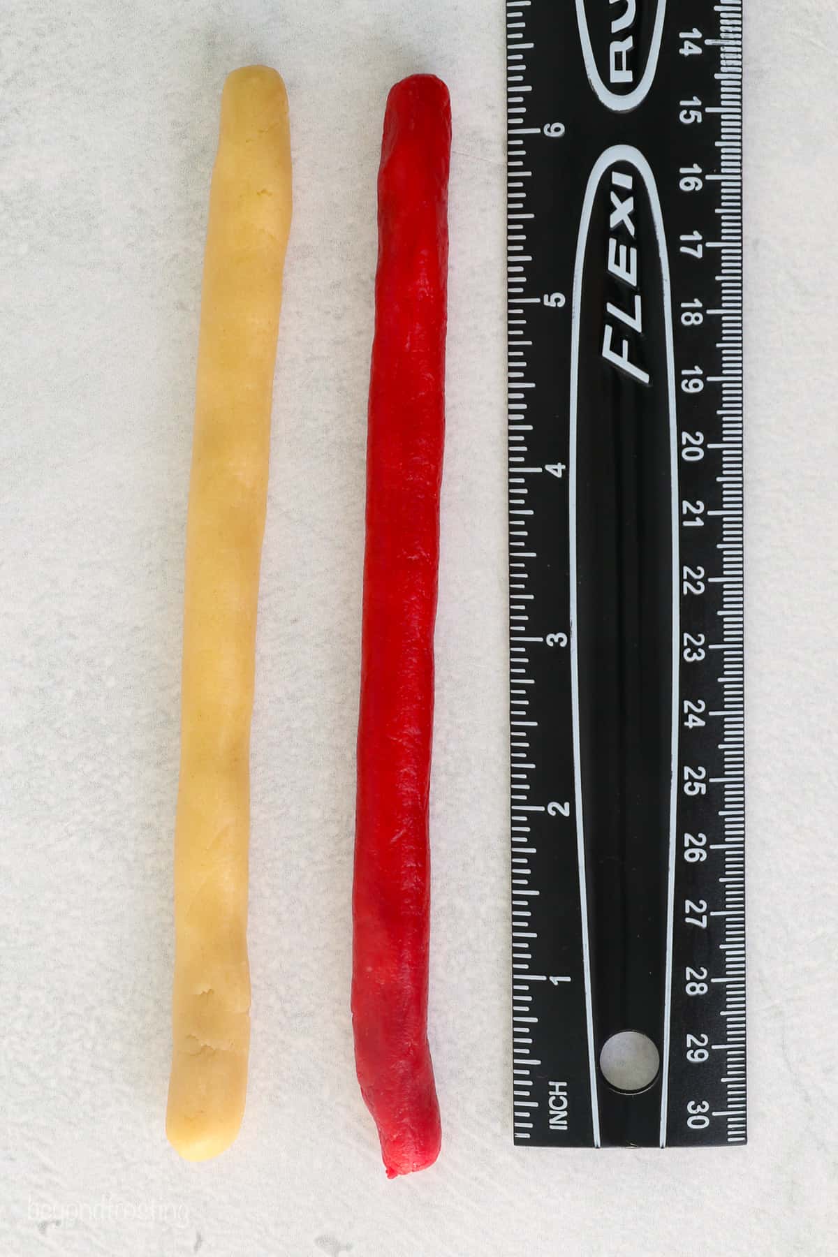 White and red sugar cookie dough ropes lined up next to a black ruler.
