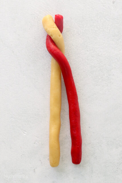 White and red sugar cookie dough ropes partially twisted together.