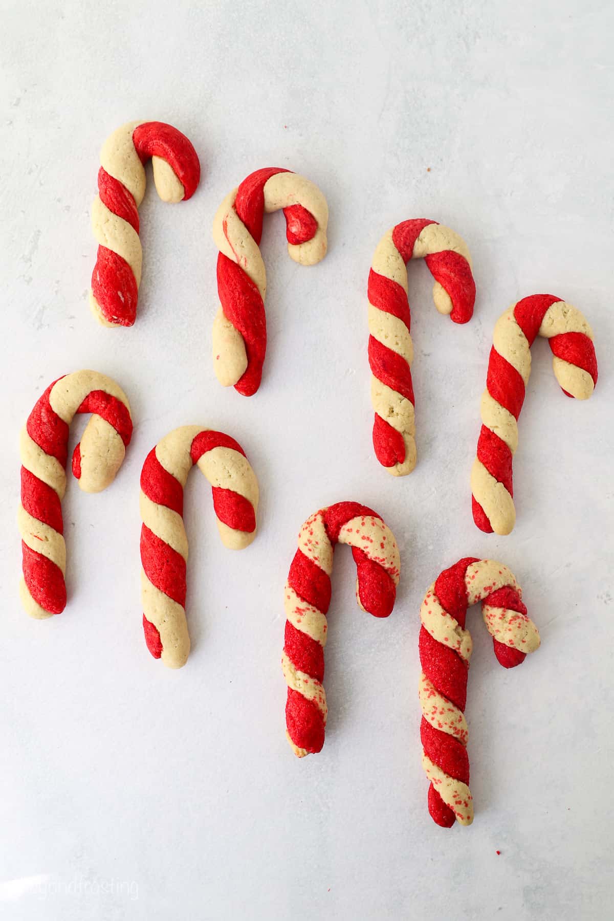 Candy cane cookies lined up in two rows on a white surface.
