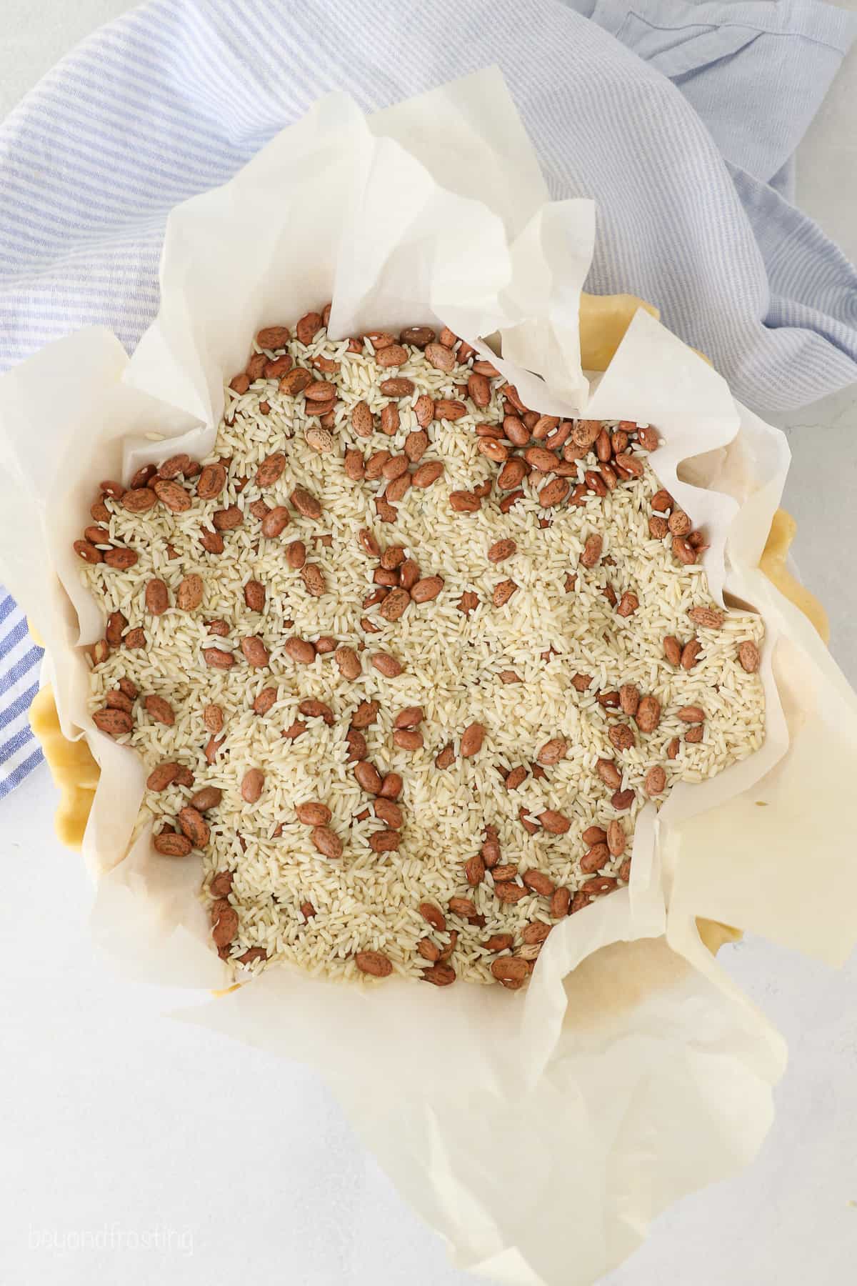 Overhead view of a pie crust lined with parchment paper filled with dry rice and beans as pie weights.