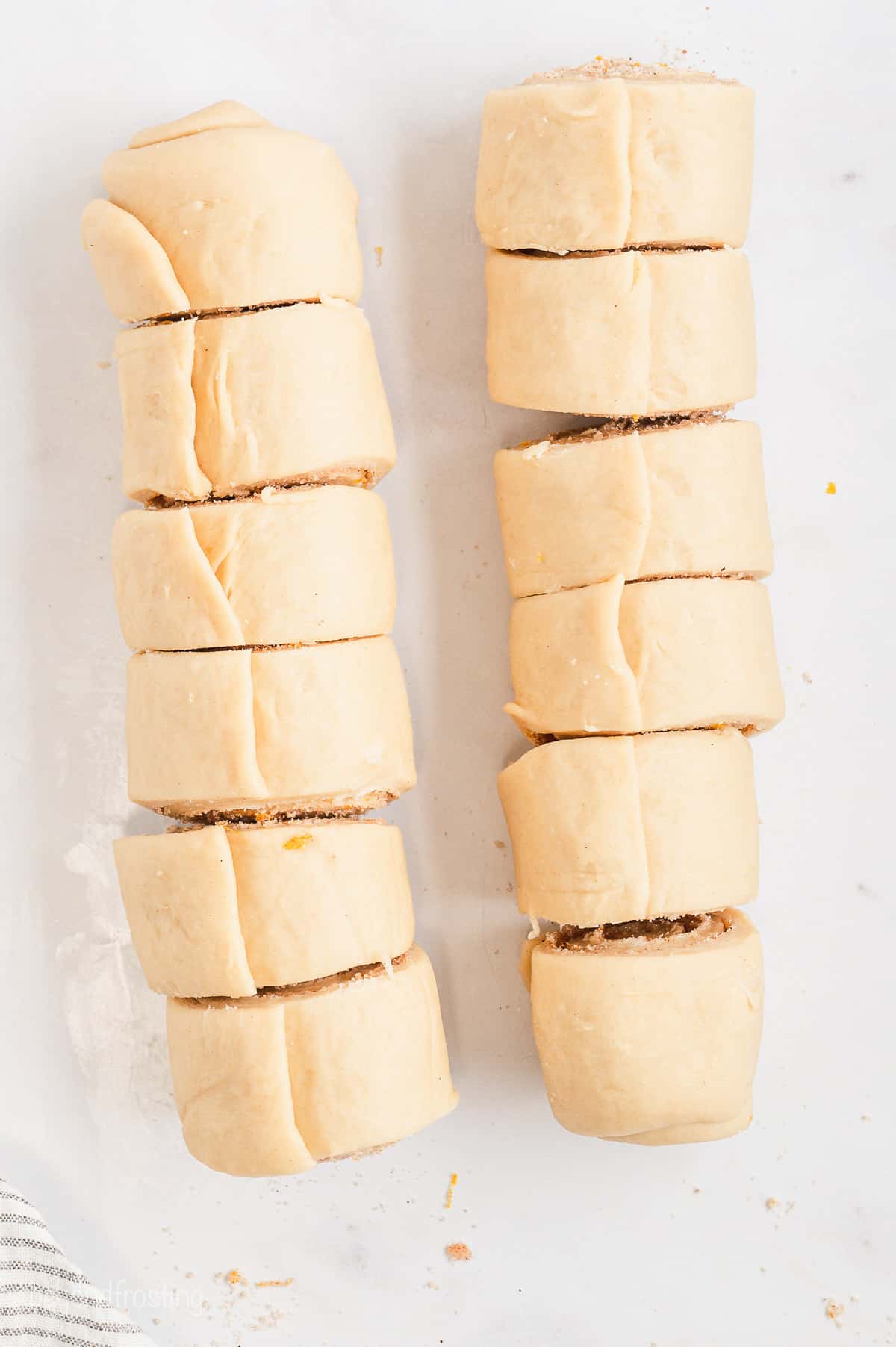 Overhead view of two logs of orange cinnamon roll dough sliced into 12 rolls.