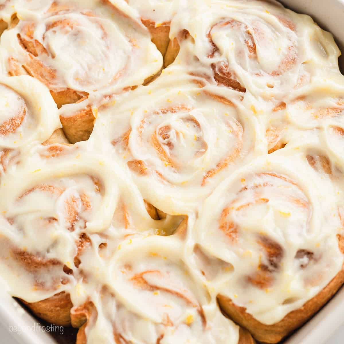 Overhead close up view of glazed orange cinnamon rolls in a white ceramic baking dish.