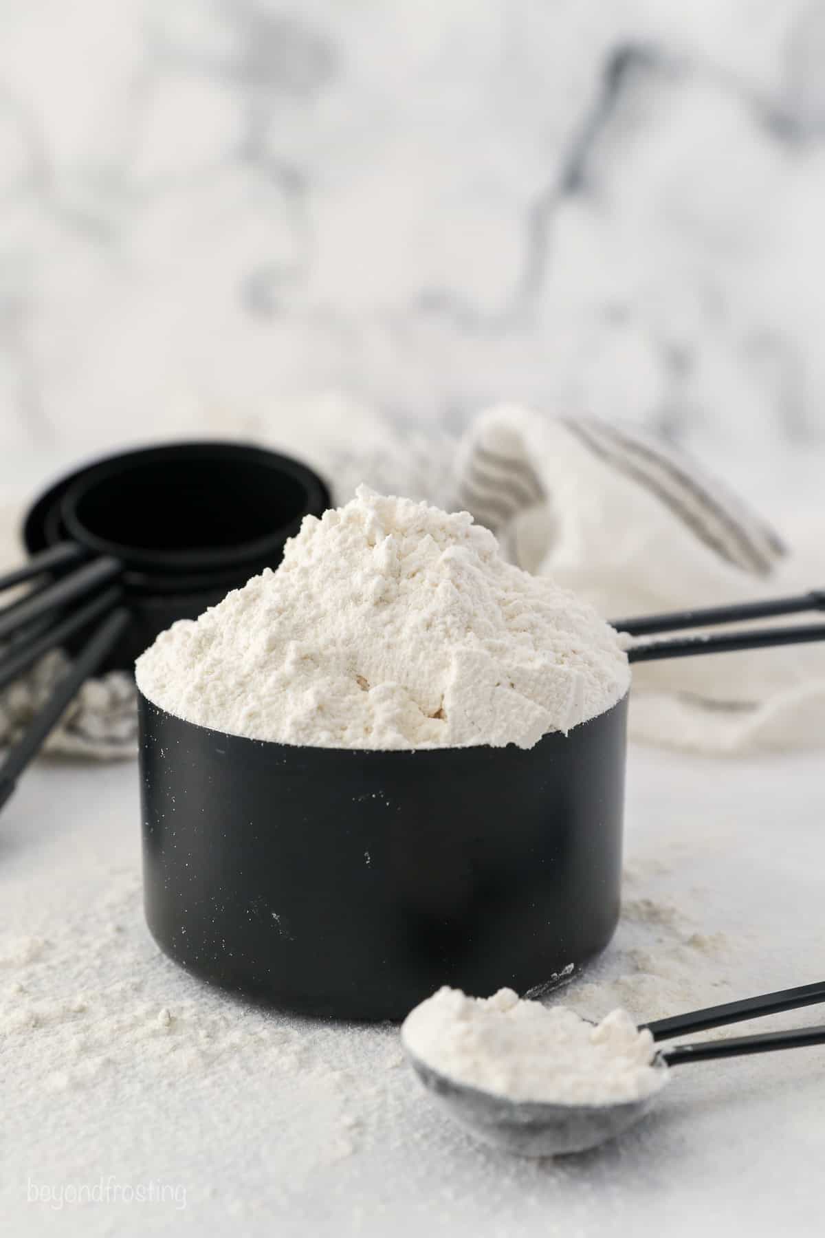 A heaping cup of flour in a black measuring cup