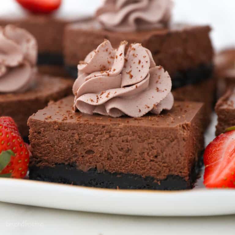 A close up of a sliced chocolate cheesecake bar on a white rimmed plate topped with chocolate whipped cream