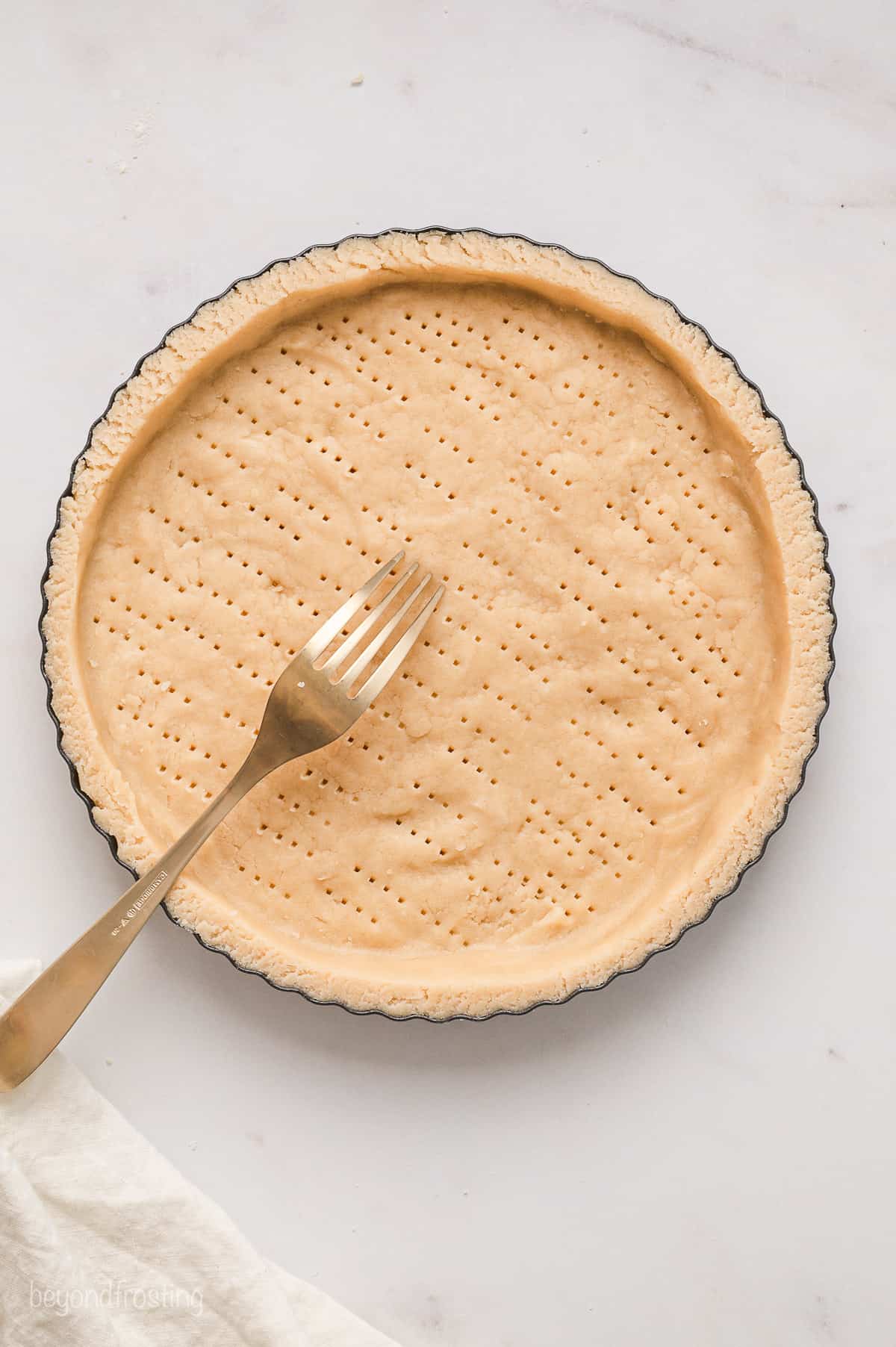 A fork is used to poke holes in the bottom of a prepared pastry shell.