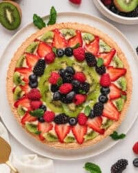 Overhead view of a fruit tart surrounded by scattered fresh fruit.