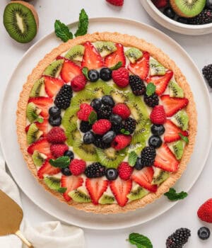 Overhead view of a fruit tart surrounded by scattered fresh fruit.