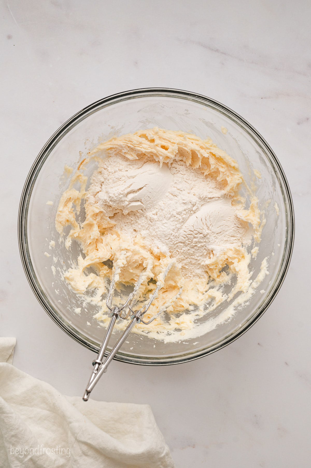 Flour added to creamed butter and sugar in a glass mixing bowl.