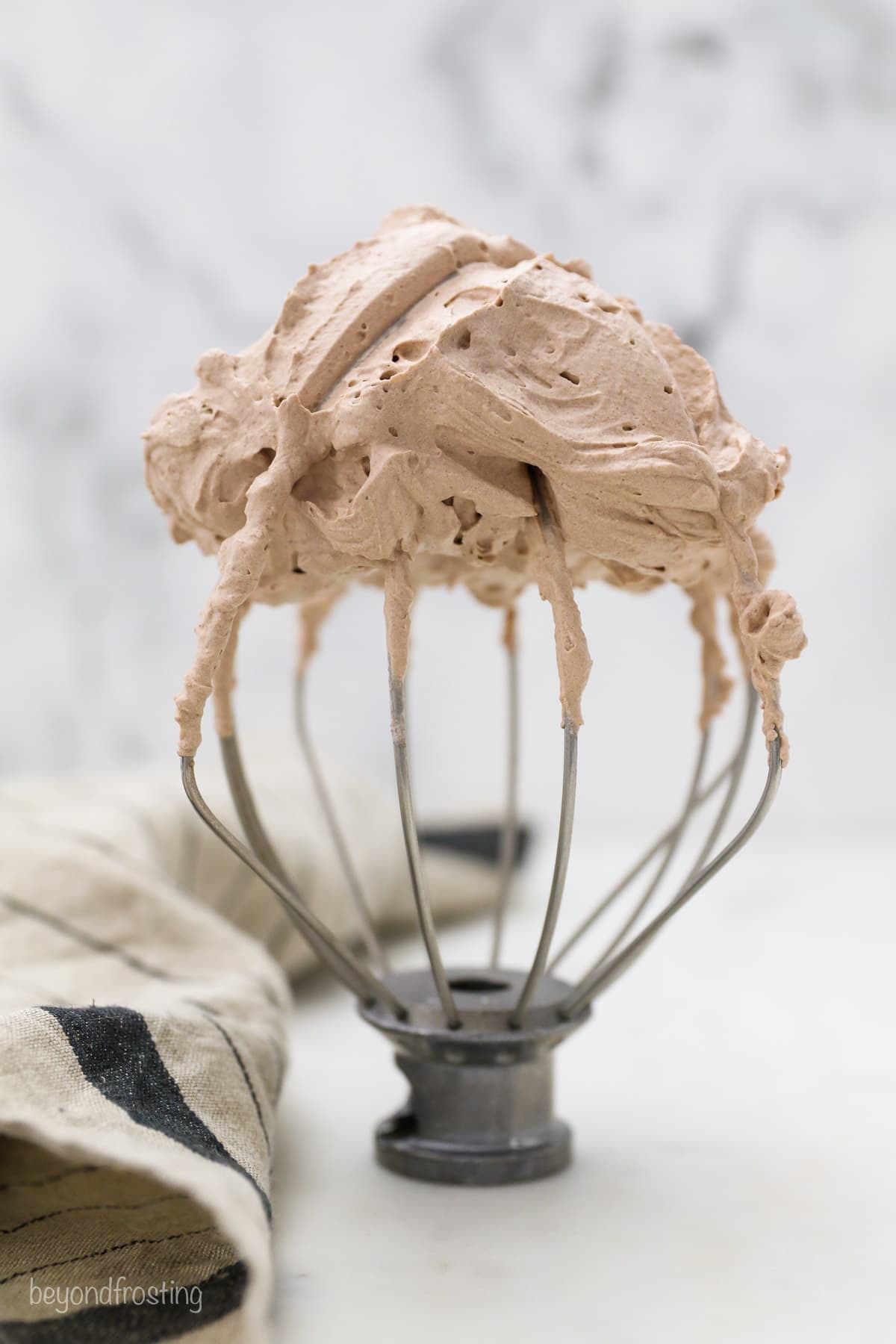A wire whisk attachment with chocolate whipped cream on top