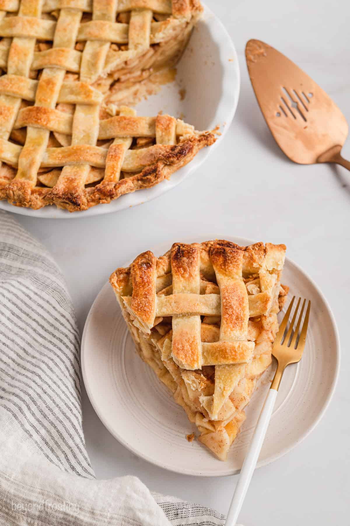 A slice of pie with a lattice crust on a white plate, with the rest of the pie in the background.