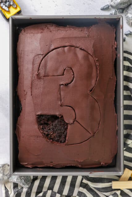 Part of the frosting removed from an outline of the number 3 traced onto a frosted chocolate sheet cake.