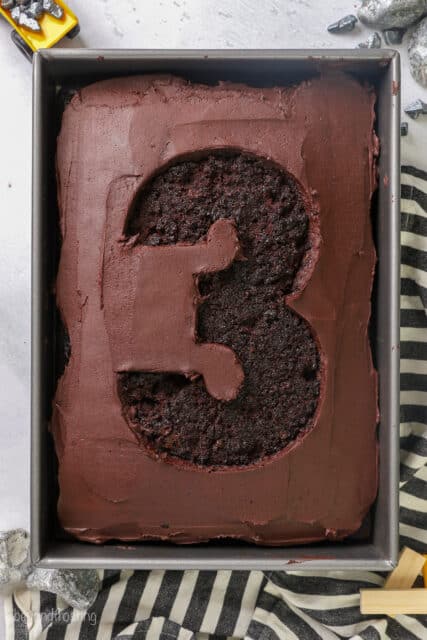 Frosting removed from an outline of the number 3 on a frosted chocolate sheet cake.