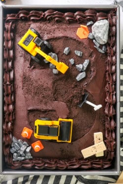 Overhead view of a construction cake with the number 3 carved into the frosting, decorated with construction activity toys, small blocks of wood, and plastic shovels.