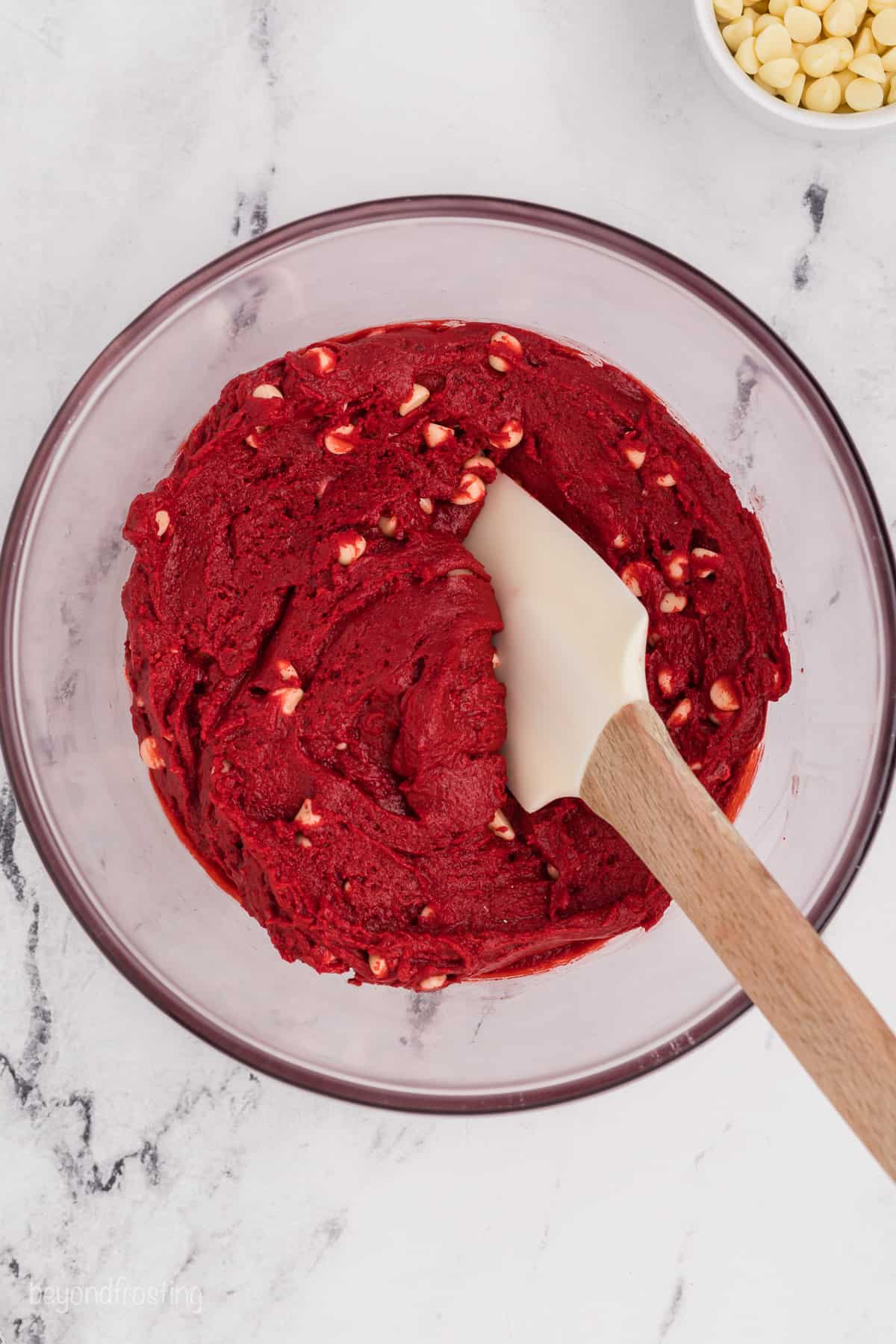 Red velvet cookie dough with white chocolate chips in a glass bowl with a spatula.
