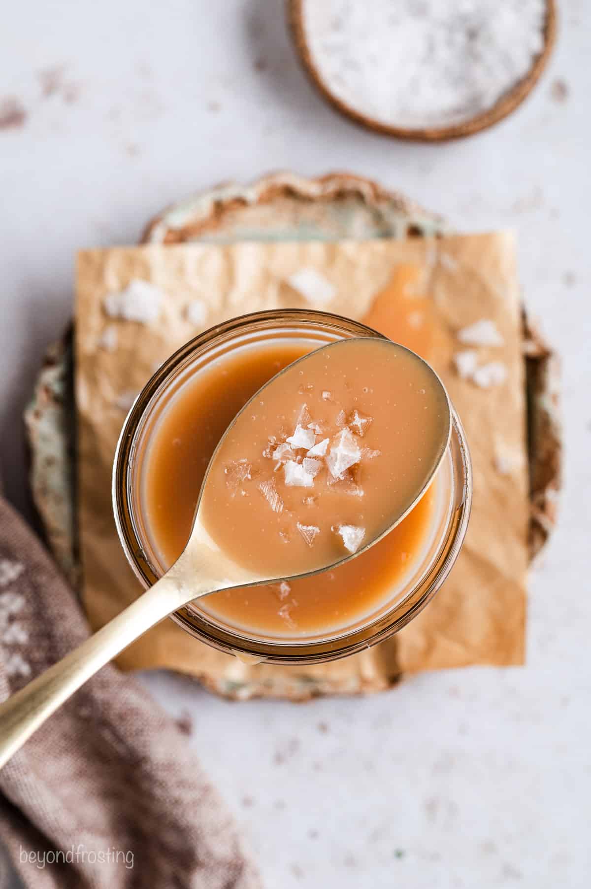 Overhead view of a spoonful of salted caramel held over a jar.
