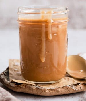 A jar of salted caramel sauce with sauce dripping down the side, next to a spoon.