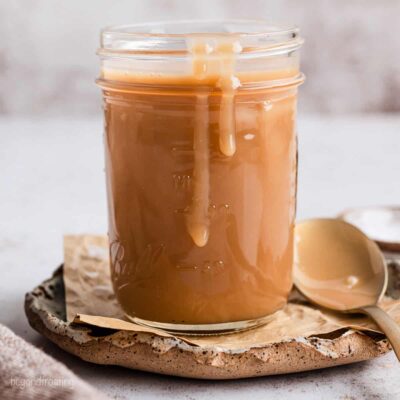 A jar of salted caramel sauce with sauce dripping down the side, next to a spoon.