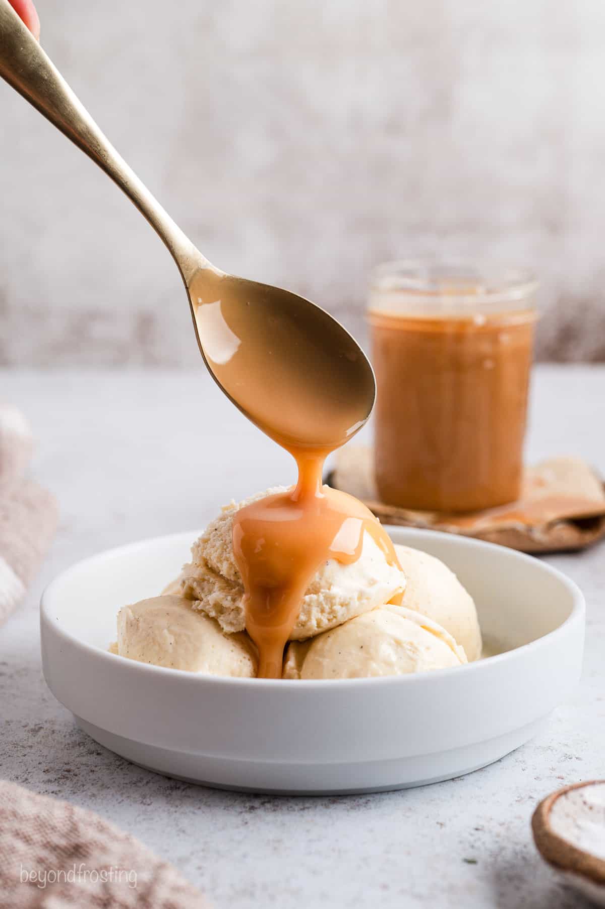 A spoon drizzling salted caramel sauce over a bowl of ice cream.