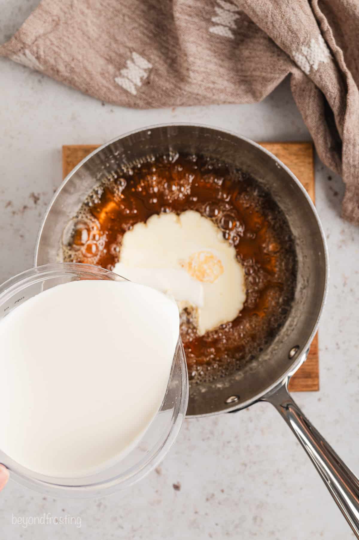 Heavy cream being poured into boiling sugar syrup in a saucepan on an induction stove.