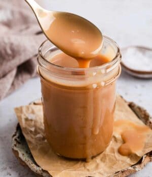 A spoon drizzling salted caramel sauce into a jar.