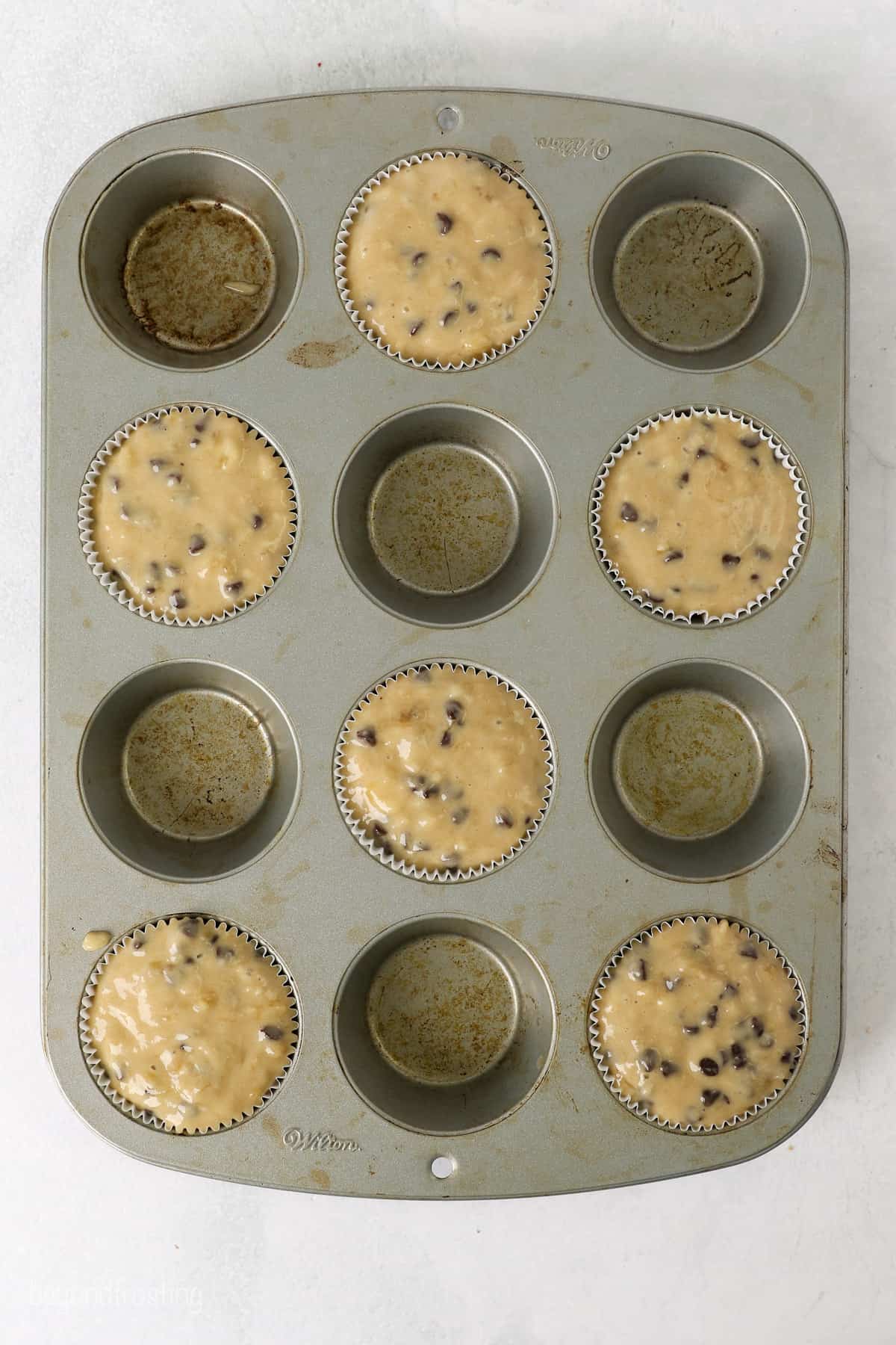 Overhead view of a 12-well muffin pan partially filled with banana chocolate chip muffin batter.