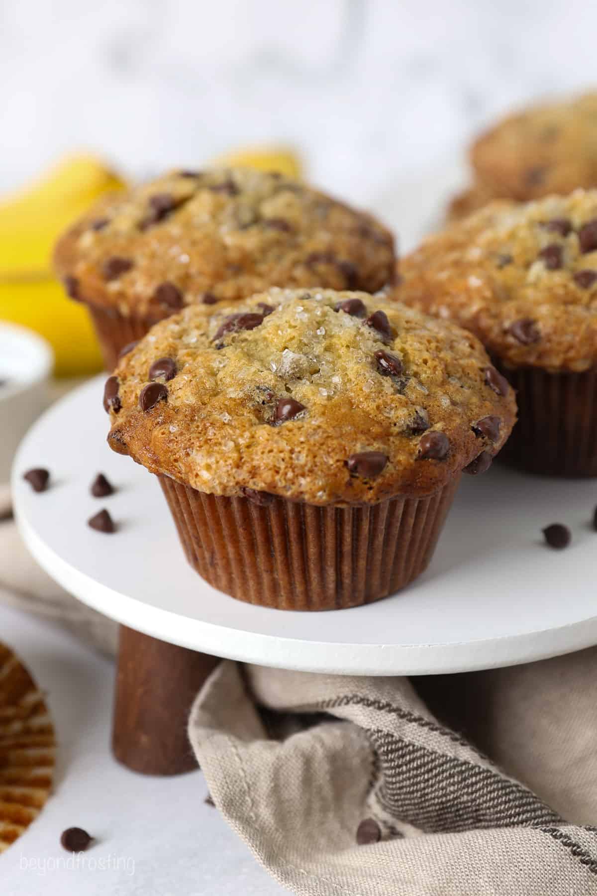 Banana chocolate chip muffins on a white cake stand.