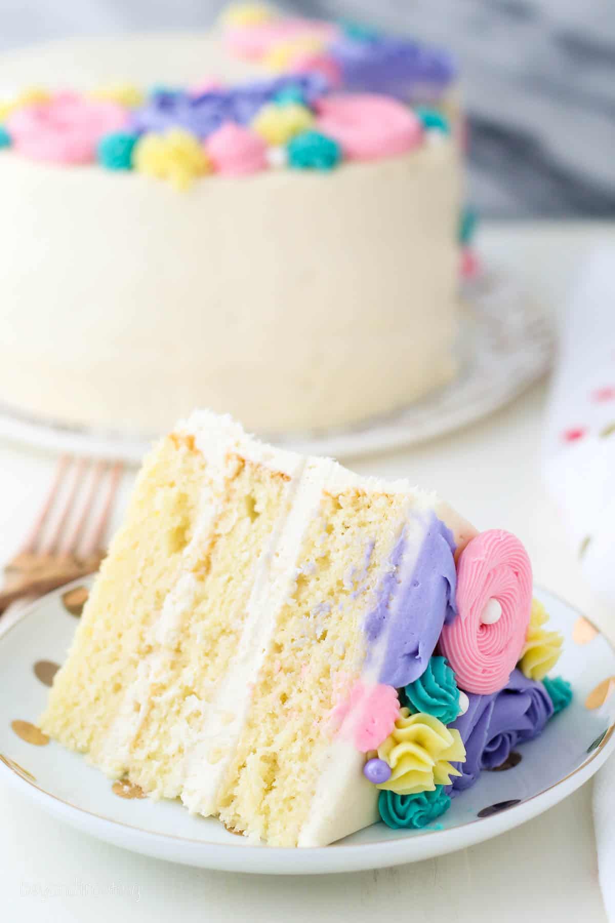 A slice of buttercream flower cake on a plate with the rest of the cake in the background.
