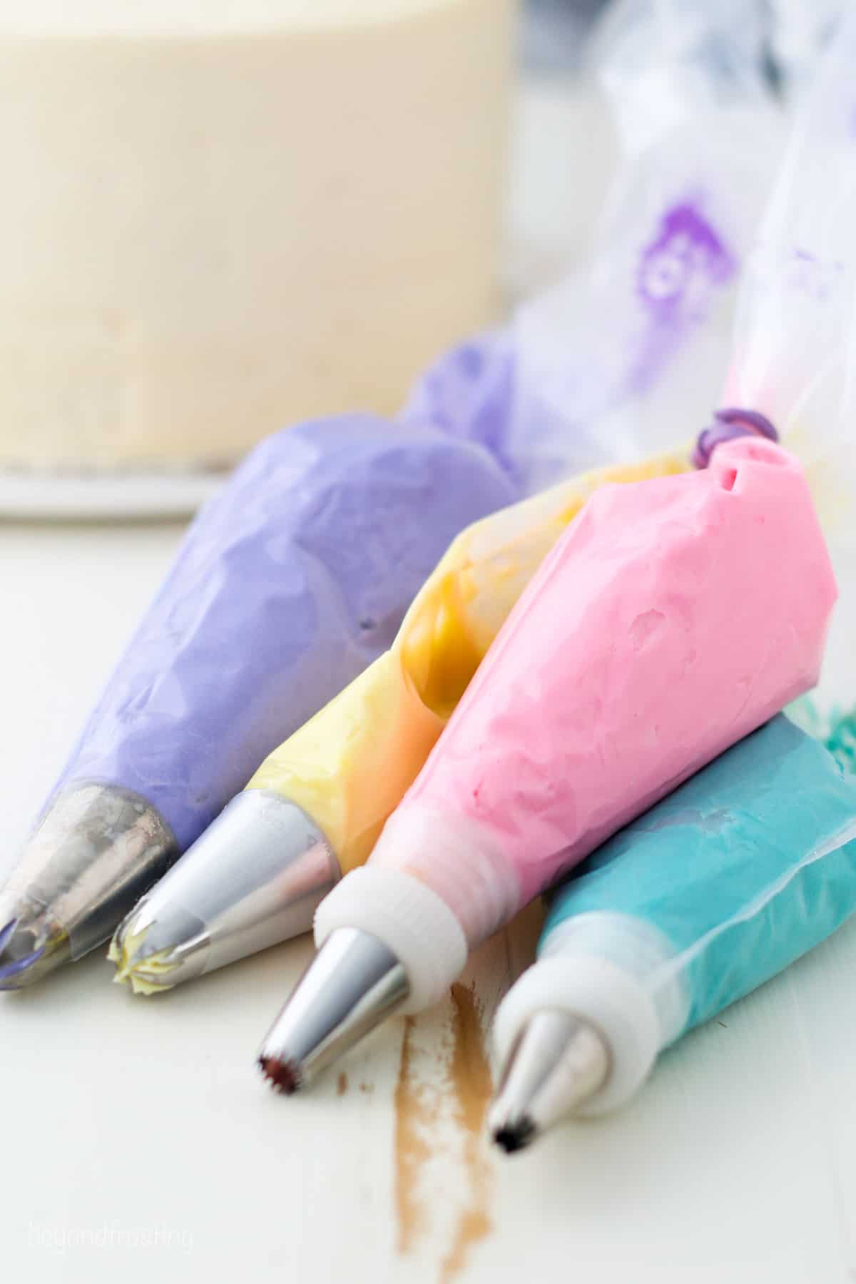Stacked piping bags filled with pastel purple, yellow, pink, and turquoise buttercream.