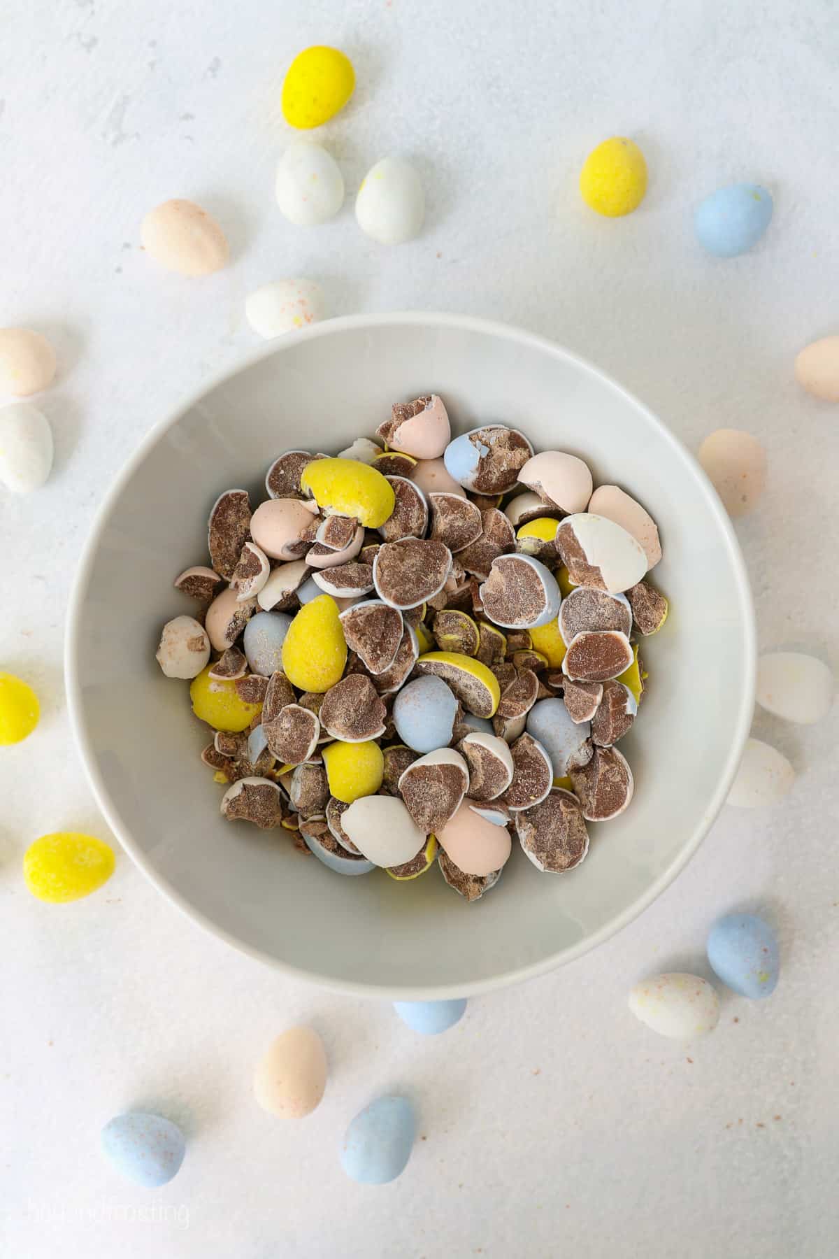 A white bowl of crushed Cadbury Mini eggs with more whole eggs laying around the bowl